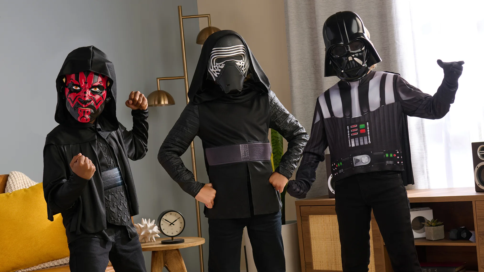 Three children wearing Star Wars villain costumes posing together indoors