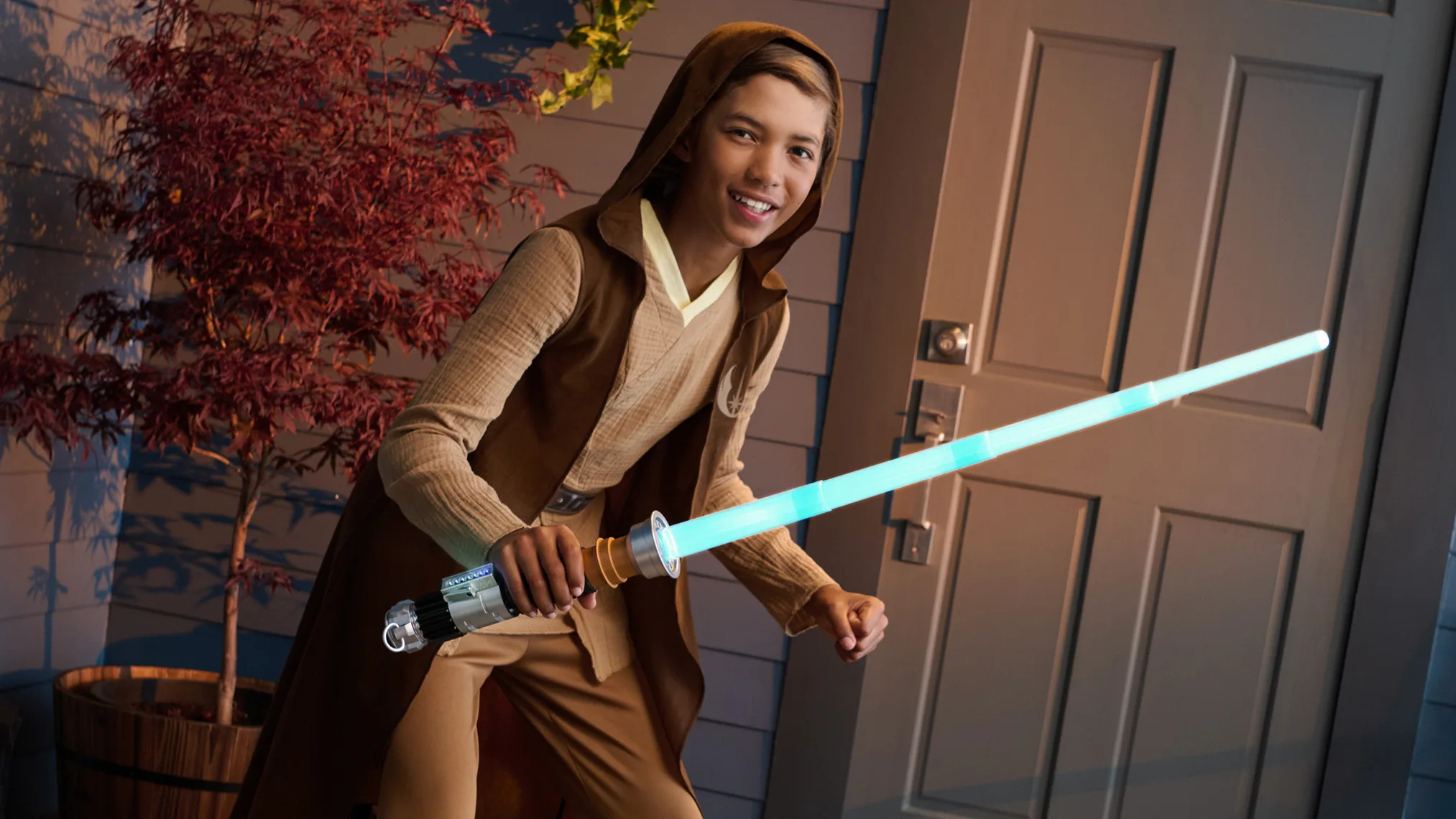 Child dressed as a Jedi holding a glowing toy lightsaber
