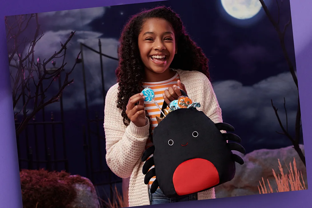 Girl holding a Squishmallows Halloween spider treat pail filled with candy