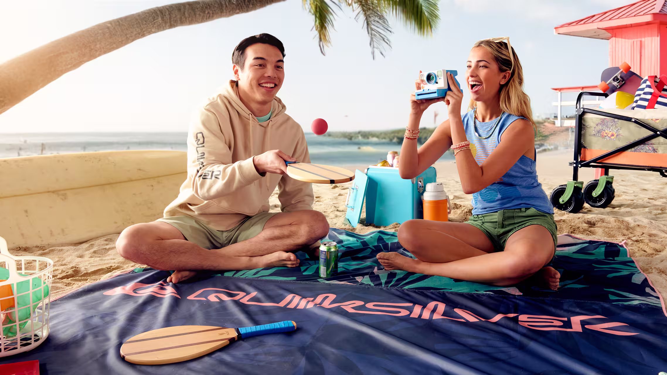 Couple playing paddle ball on a beach picnic blanket