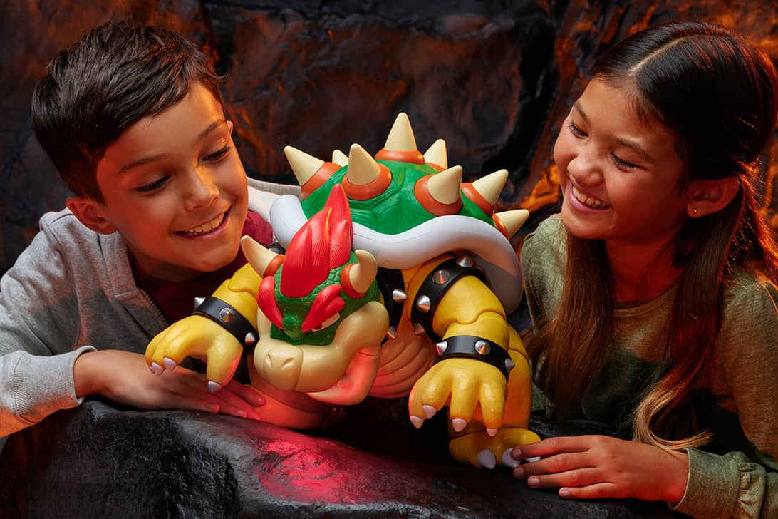Kids playing with Bowser action figure toy from Super Mario in dramatic lava environment