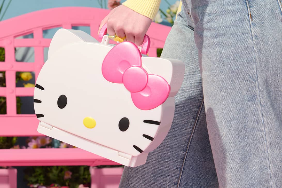 Person carrying Hello Kitty shaped toy case with pink bow near pink bench