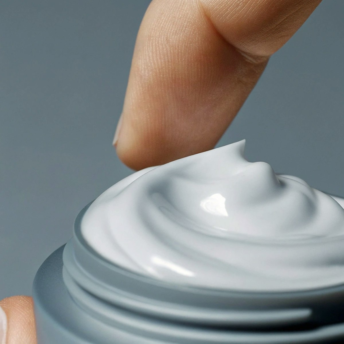 En finger, der dypper ned i en krukke med hvid, cremet hudplejeprodukt.