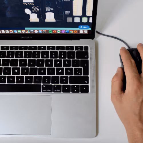 Hånd der bruger en kablet mus ved siden af et MacBook Air tastatur med skærm, der viser forskellige kosmetikprodukter.