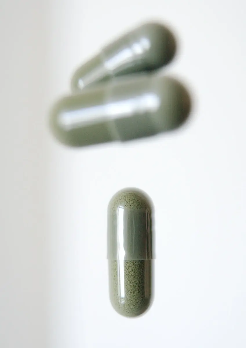 Nærbillede af grønne medicinkapsler på hvid baggrund.