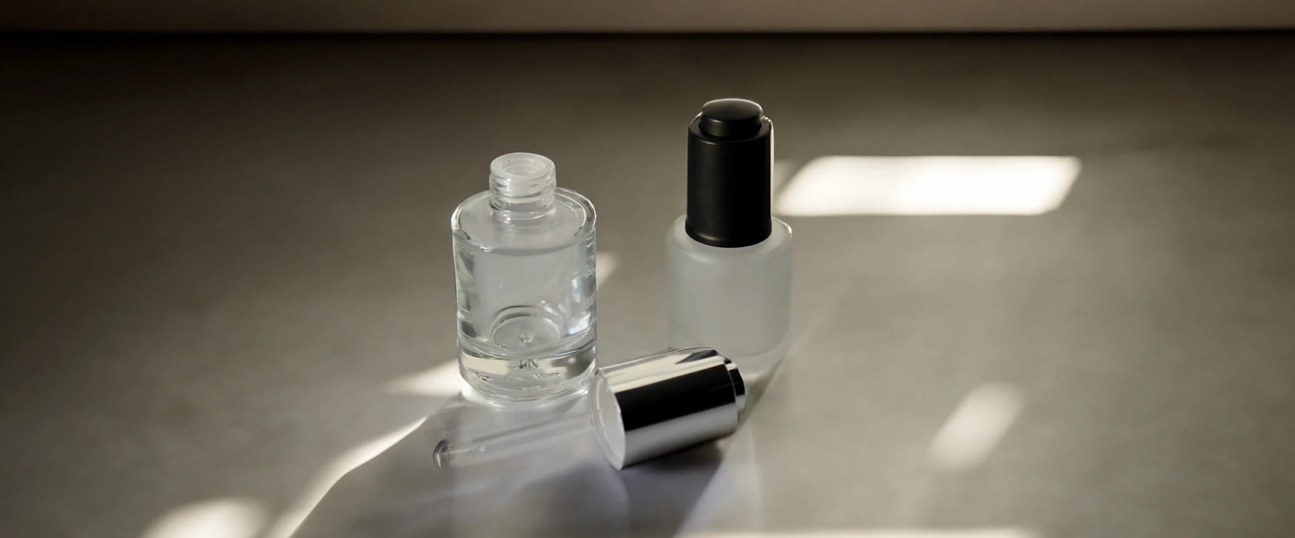 To glasflasker til dråber, hvor den ene er åben med en dråber ligger ved siden af på en lys overflade.