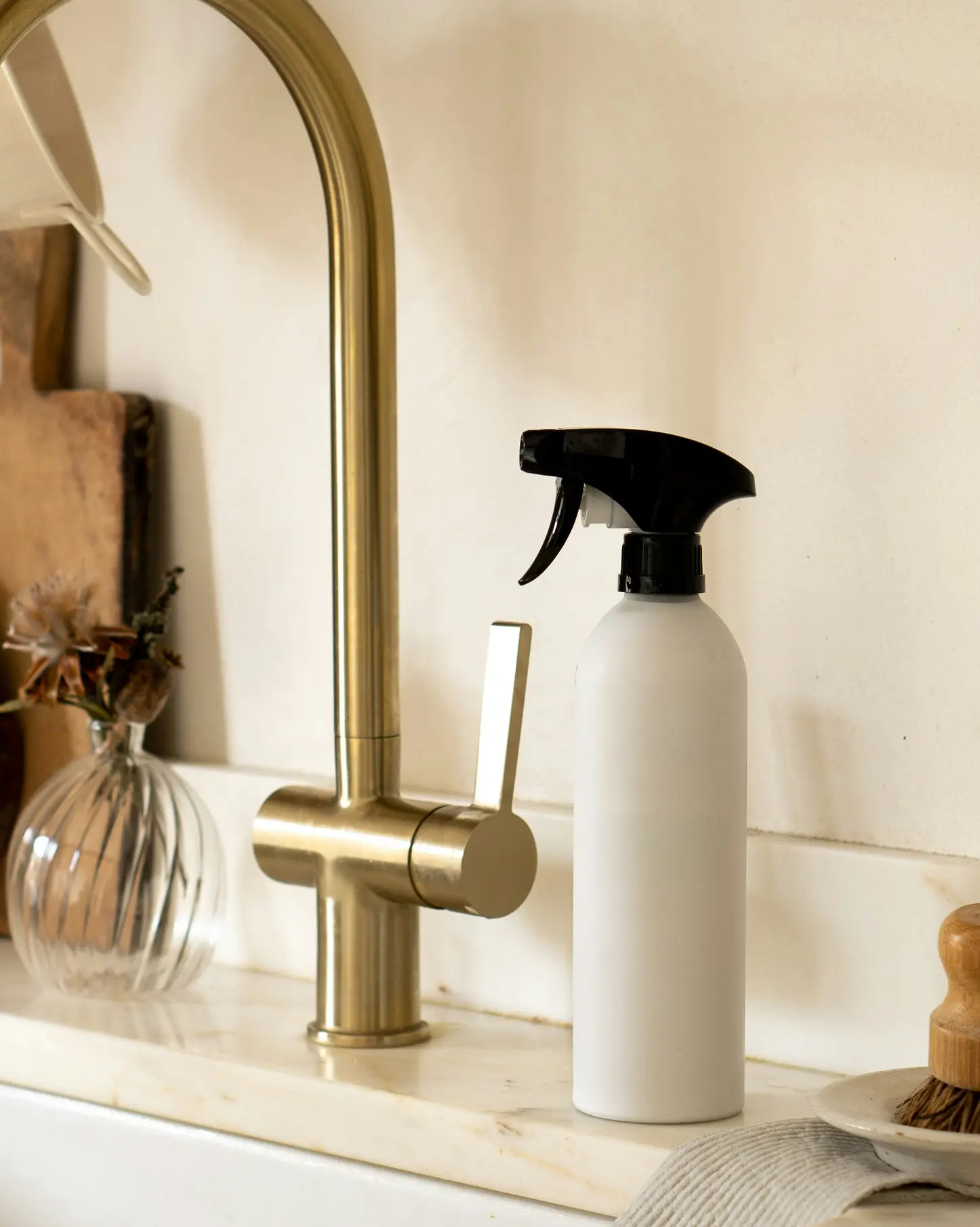 Hvid sprayflaske med sort spids ved siden af messingvandhane på marmorvask.
