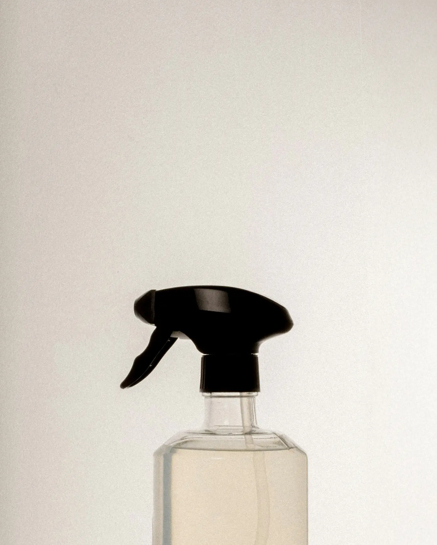 Sprayflaske med gennemsigtig væske og sort udløser mod lys baggrund.