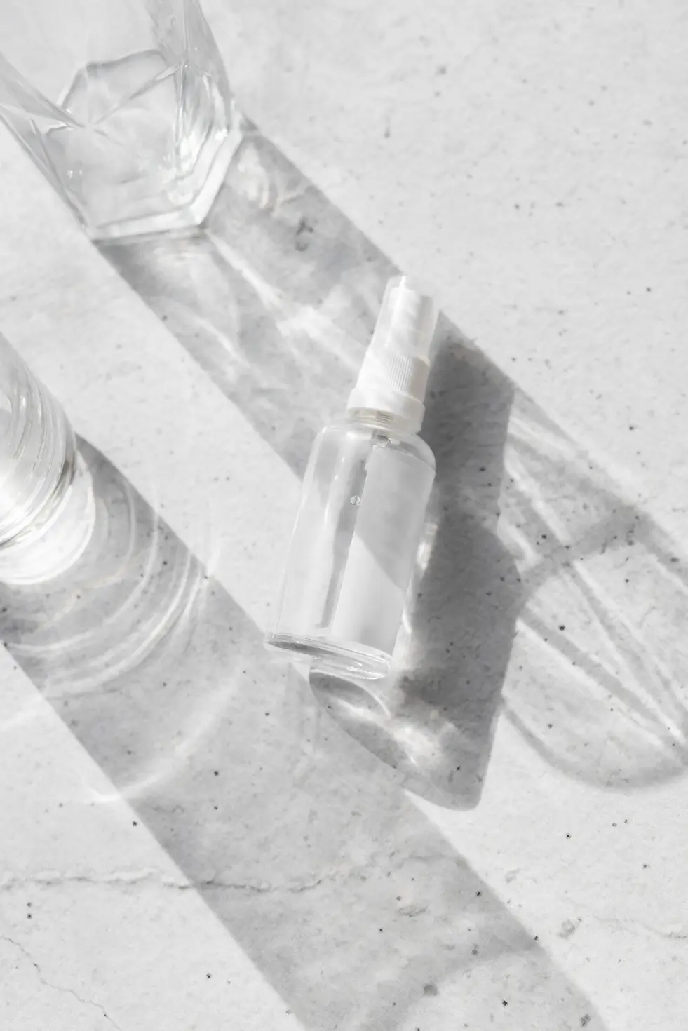 Sprayflaske liggende på en lys overflade med sollys og skygger.