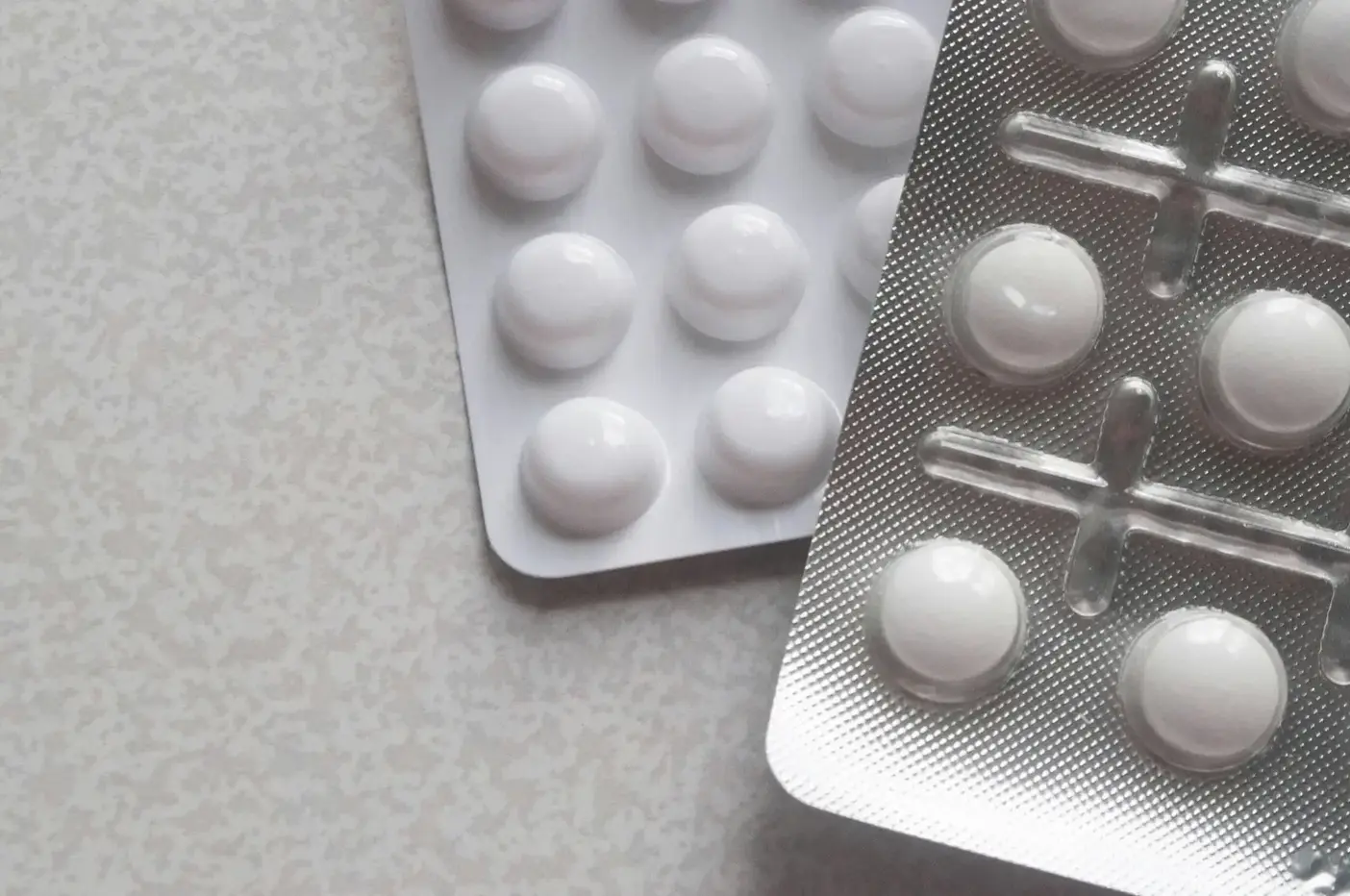 To blisterpakker med hvide runde tabletter på en lysegrå bordplade.