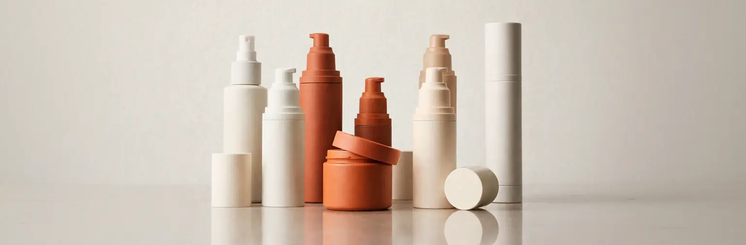 Emballager i hvide og orange farver arrangeret på en refleksiv overflade mod en neutral baggrund.