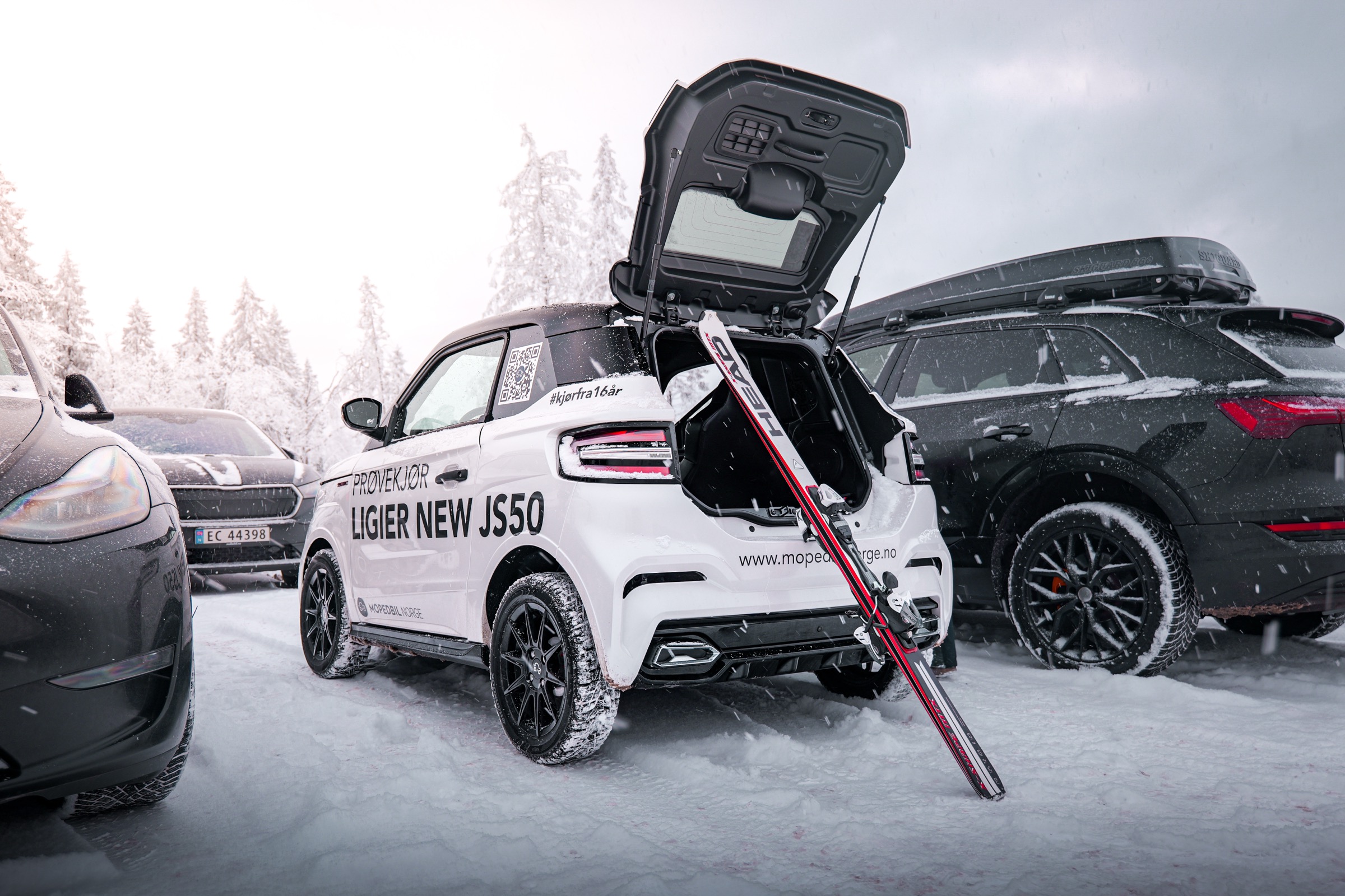 Hvit Ligier JS50 med åpen bagasjeluke og ski, parkert i snøen