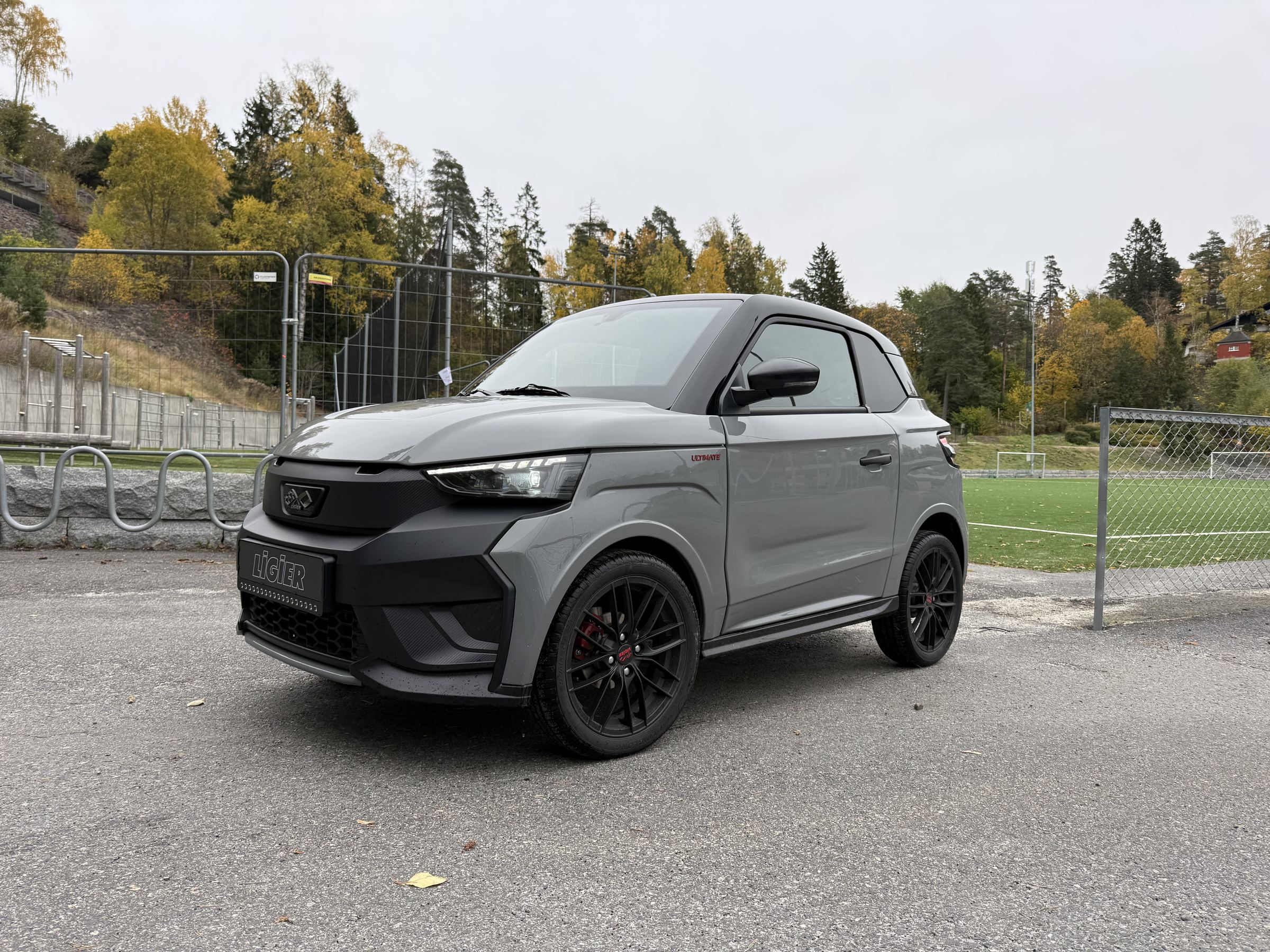 Grå Ligier JS50 EV parkert ved en fotballbane