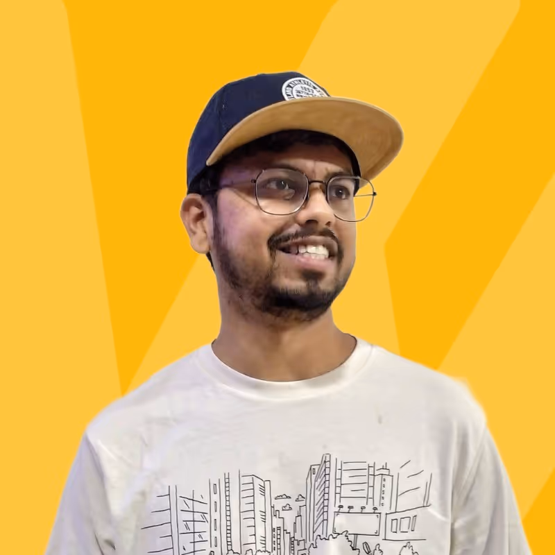 Smiling man with glasses and a black and beige cap wearing a white t-shirt with a cityscape design on a yellow background.