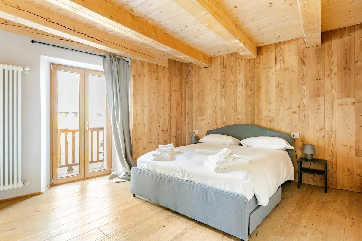 Schlafzimmer mit Holzwand und Balkon in einer von Imoreo betreuten Ferienwohnung in Courmayeur