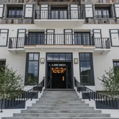 Entrée de l'Écrin de Megève avec de larges marches en pierre, des balustrades noires, de grandes fenêtres et un lustre éclairé à l'intérieur.