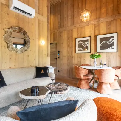 Salon moderne et confortable avec des murs en bois, un canapé beige, deux tables basses rondes en marbre, des chaises orange autour d'une table et des décorations murales.