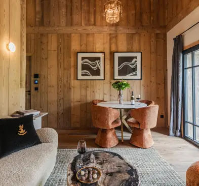 Coin repas avec deux chaises en velours orange autour d'une petite table ronde, décor chaleureux en bois avec un canapé beige et un tapis clair sous une table basse en bois naturel.