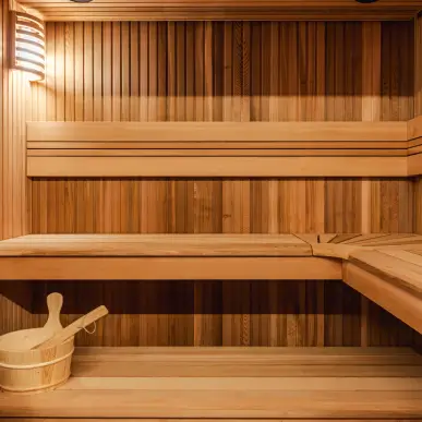 Intérieur d'un sauna en bois avec un seau en bois et une louche sur le banc inférieur, éclairage doux sur le mur.