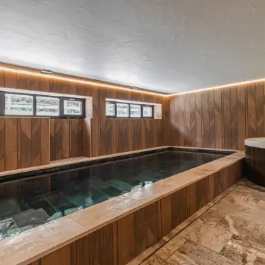 Piscine intérieure rectangulaire avec murs en bois et sol en pierre, éclairage LED encastré.