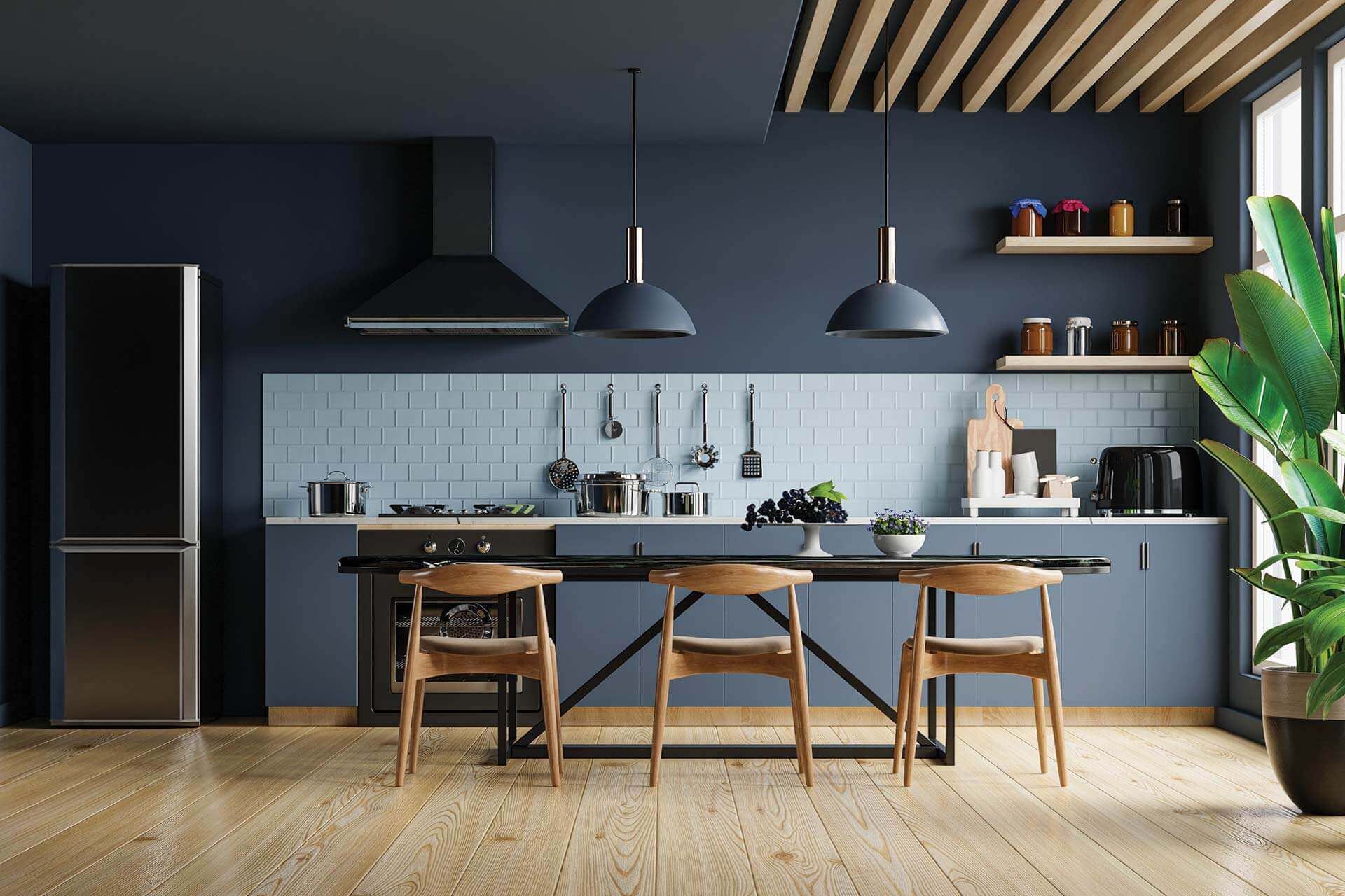 Modern kitchen with blue cabinets, black appliances, wooden chairs at a black table, and a large green plant near the window.