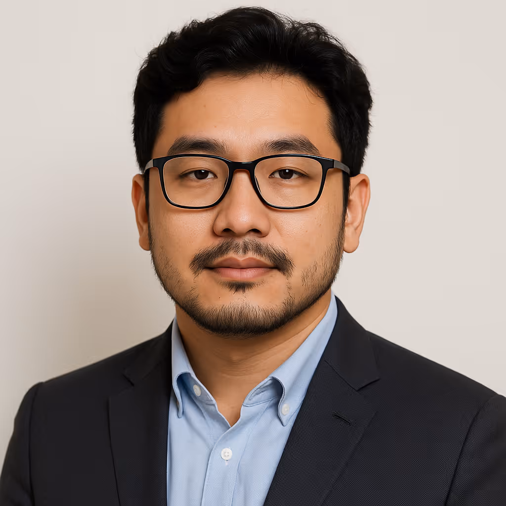 Portrait of a man with black hair and beard wearing glasses, light blue shirt, and dark blazer.