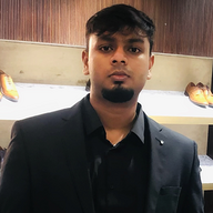 Man with short dark hair and goatee wearing a black blazer and shirt standing indoors with shoes displayed in the background.