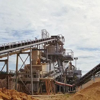 Industrial conveyor belts and machinery processing dirt or sand under a cloudy sky.