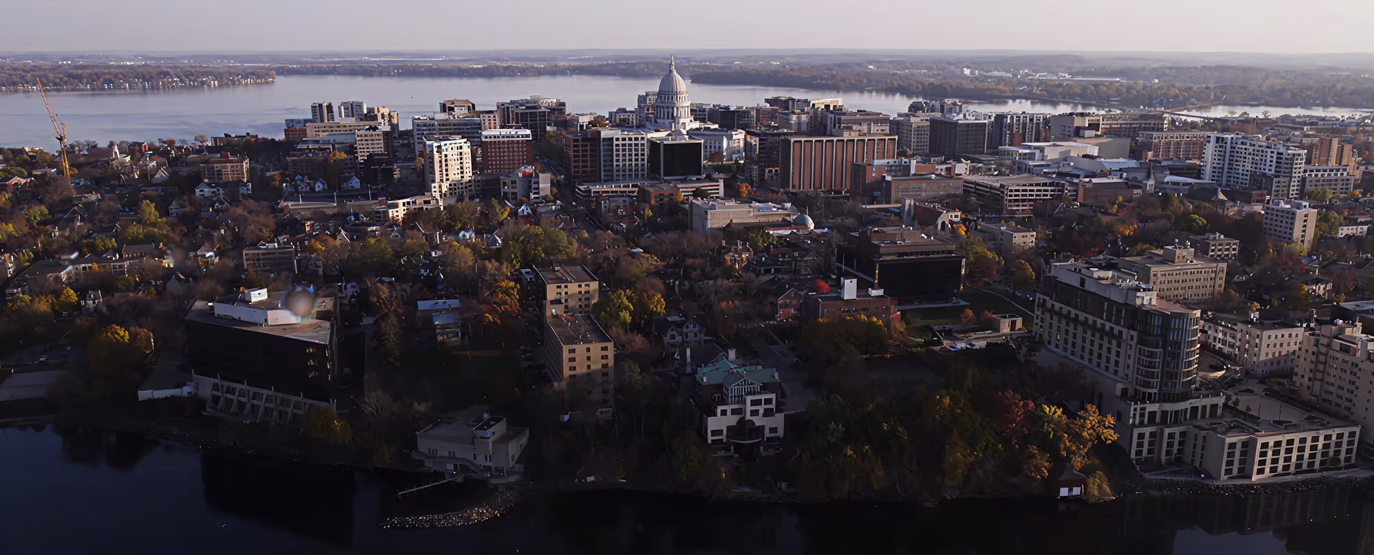 Aerial view of a cityscape with a prominent domed capitol building near a large body of water in the background.