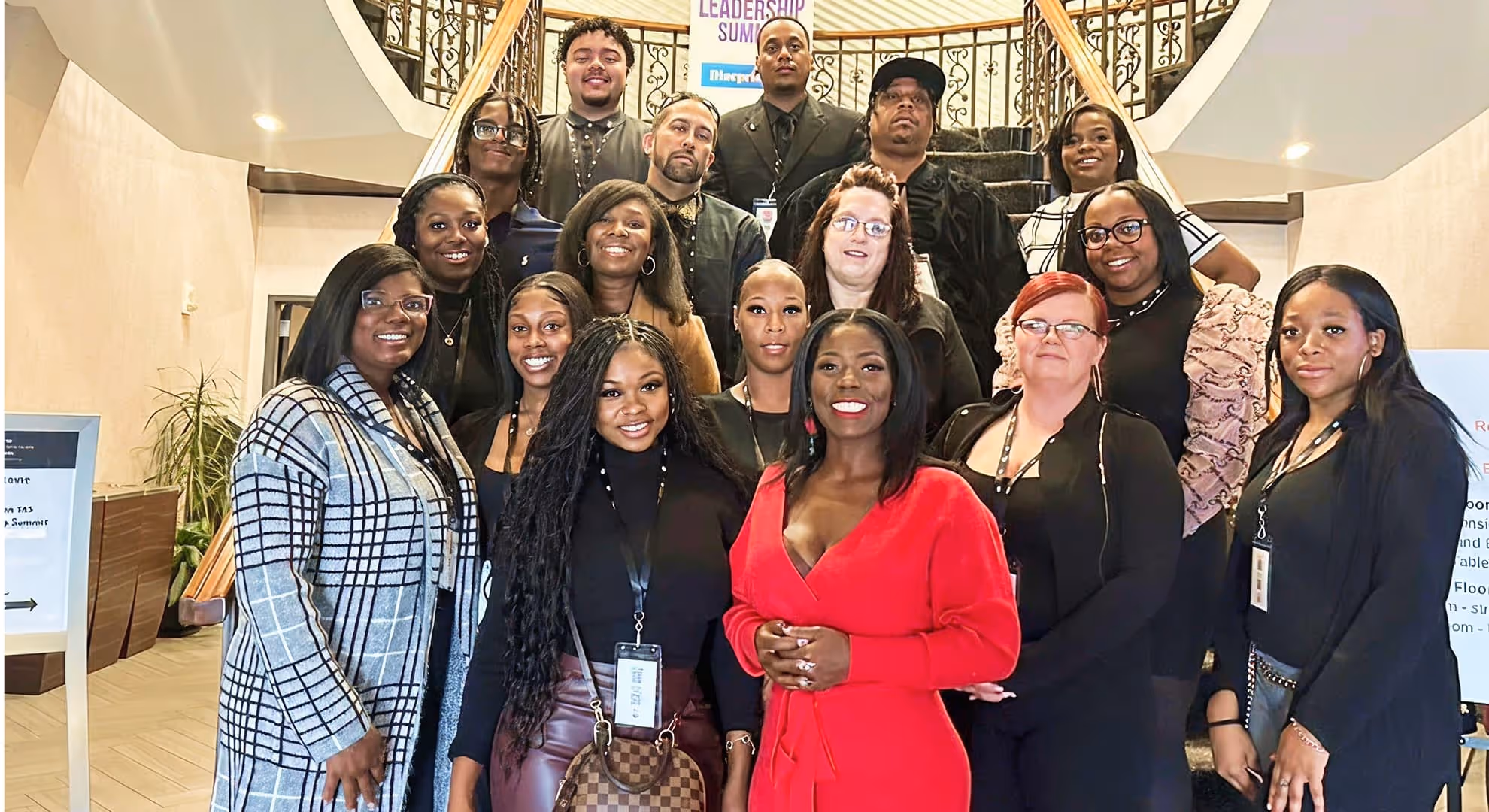 Group of diverse adults, mostly women, posing on and in front of a staircase inside a building.