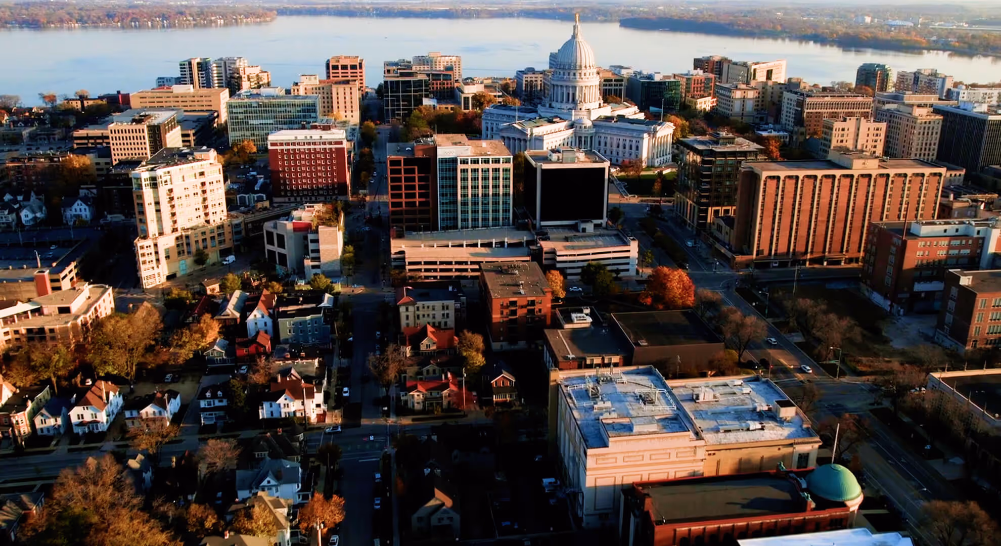 Aerial view of a cityscape featuring a prominent white domed capitol building near a large river.