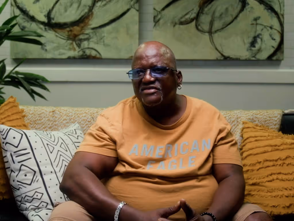 Man wearing an American Eagle t-shirt and glasses sitting on a couch with patterned and textured pillows.