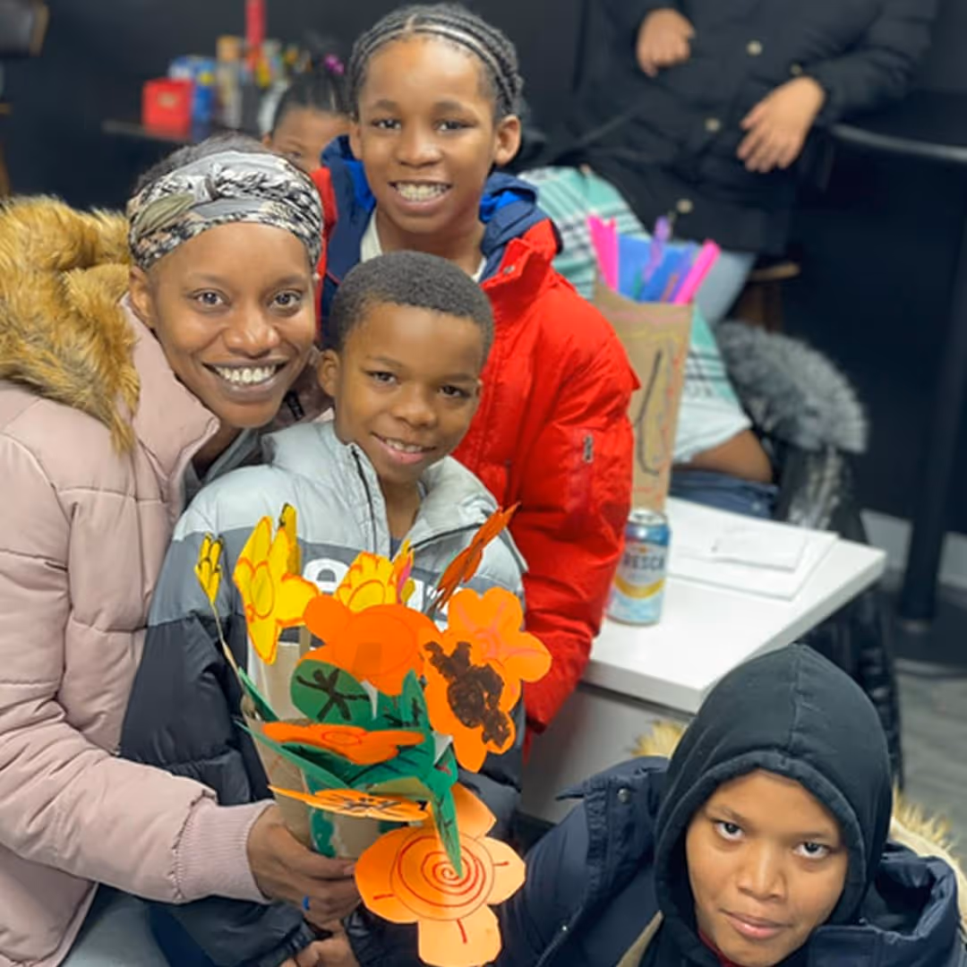 Smiling woman with three children holding colorful paper flowers indoors.