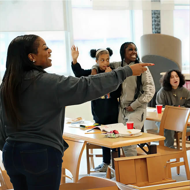 Facilitator engaging youth in an interactive group activity indoors, with participants raising hands and smiling.