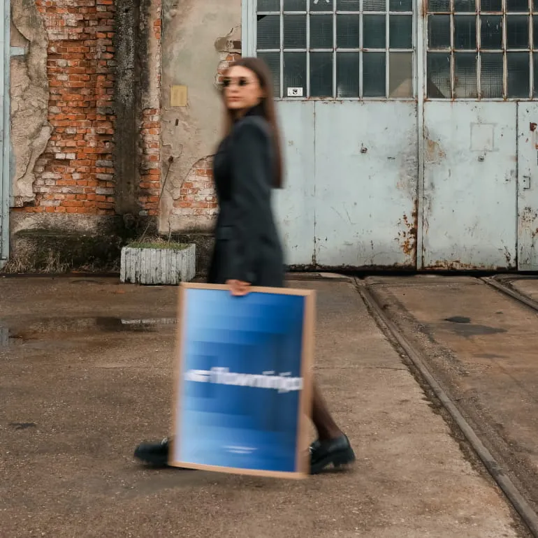 Two men working on laptops at a shared desk with plants and computer monitors near a window.