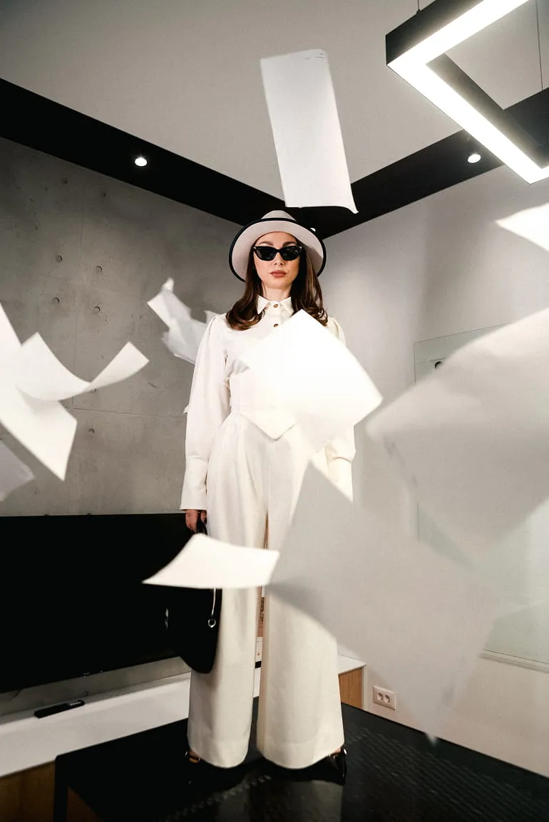 Two men working on laptops at a shared desk with plants and computer monitors near a window.