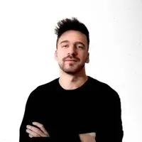 Smiling man with short dark hair wearing a black shirt against a white background.