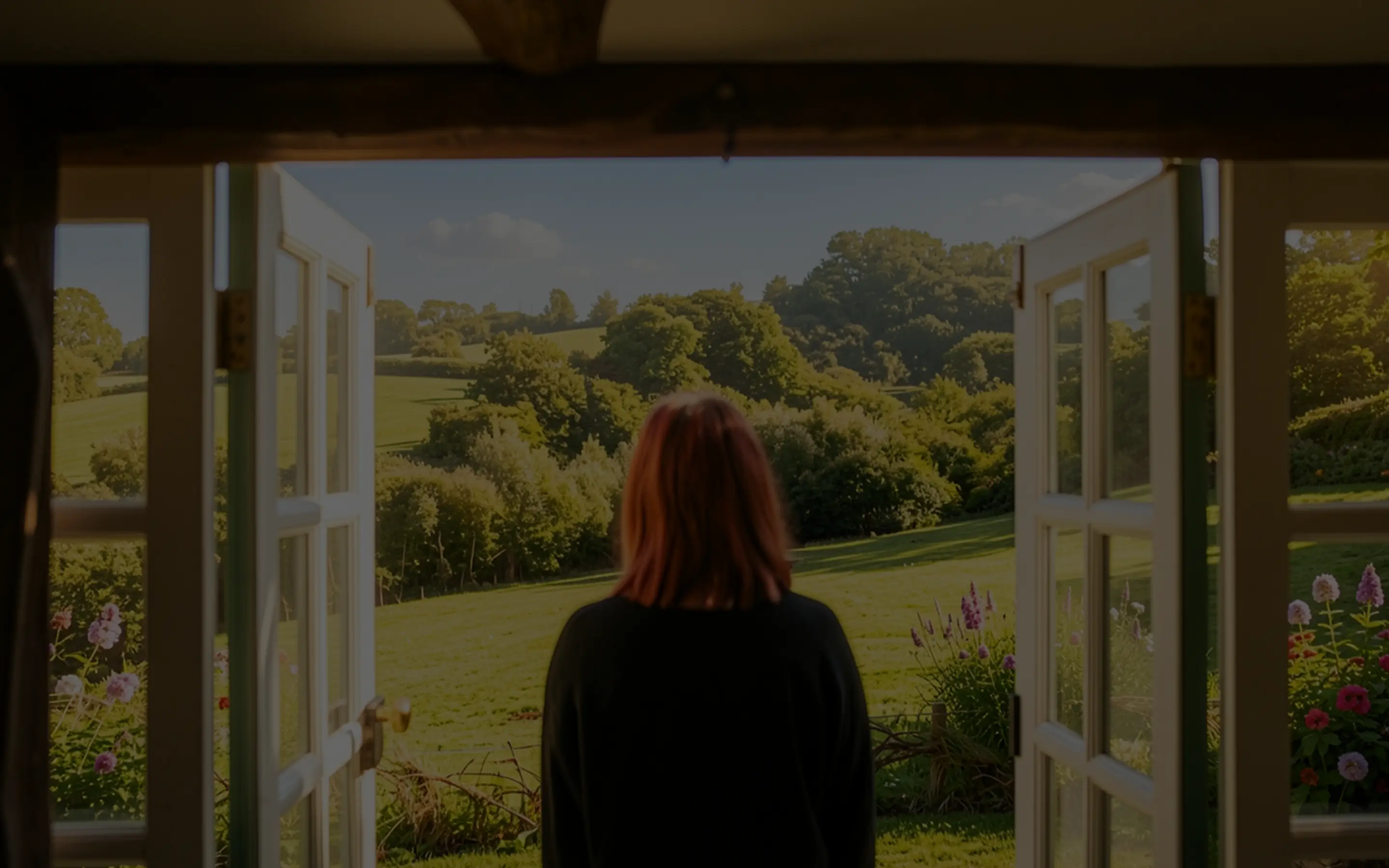 A person standing in an open doorway looking out over a sunlit green meadow, stepping from darkness into light