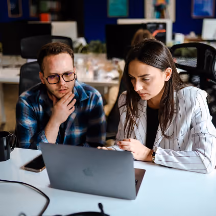 Two people working on laptops having a discussion in a modern office setting.