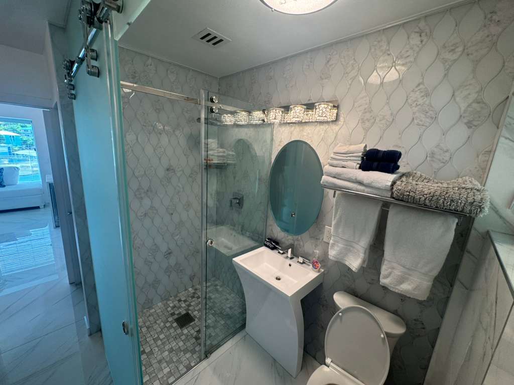 Modern bathroom with glass shower and marble tile at DGMI Properties apartment St. John.”