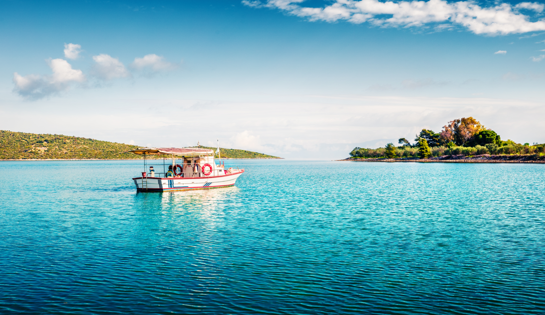 Small boat floating on clear blue water near two green islands under a partly cloudy sky.