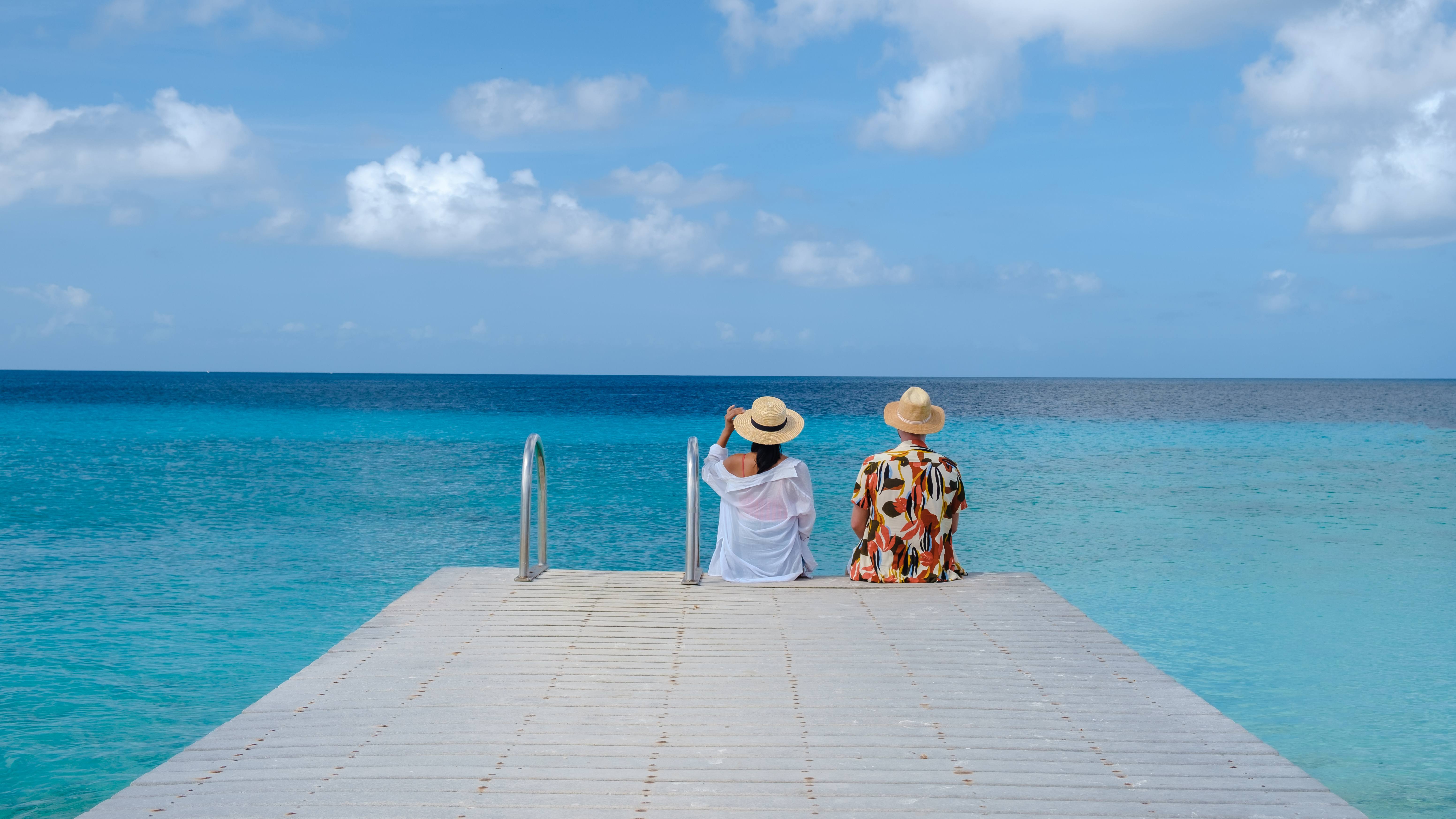 Couple relaxing on pier over turquoise Caribbean water in Cruz Bay St. John near DGMI Properties luxury suites.