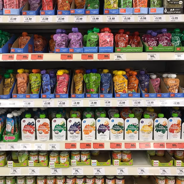 Supermarket shelf stocked with various flavors of Little Freddie baby food pouches and jars, labeled with prices and nutritional info.