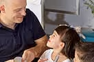 Piers from Little Freddie smiling and interacting warmly with a young girl with pigtails indoors.