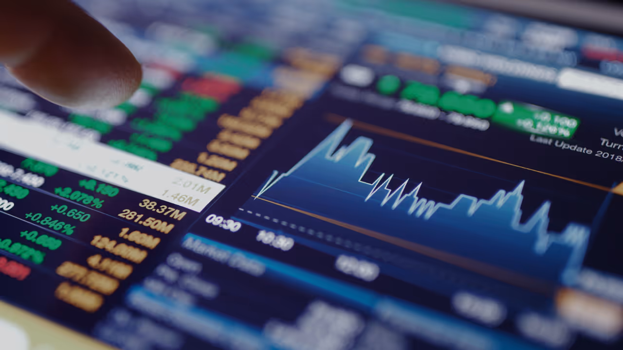 Close-up view of a finger pointing at a digital stock market chart with fluctuating lines and numbers in green and gold.