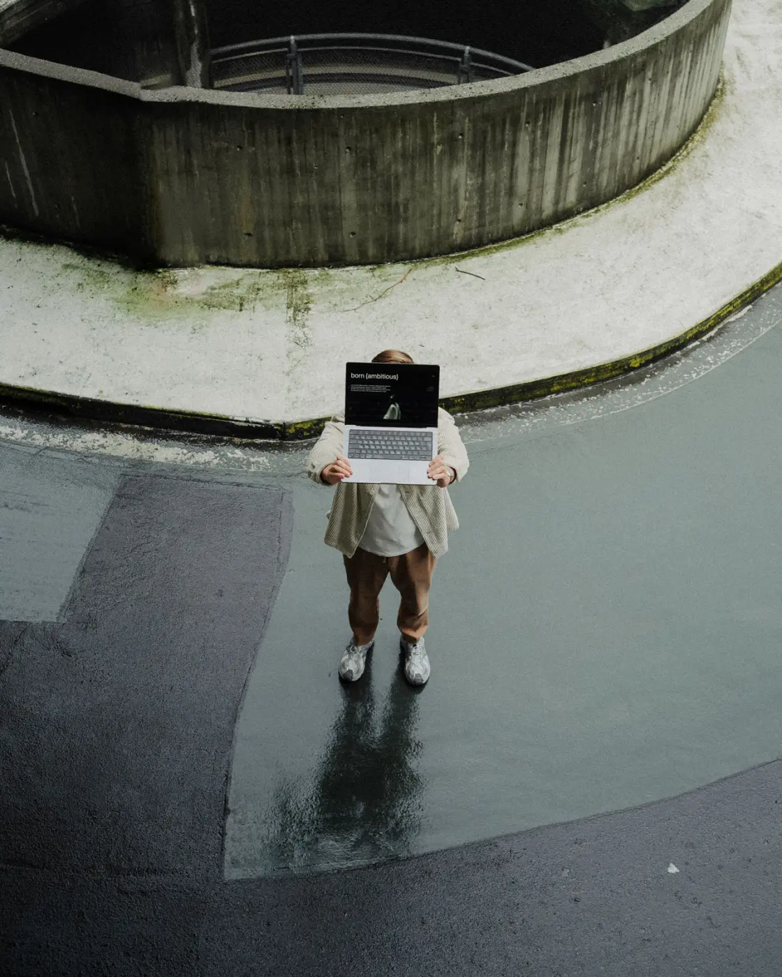 En person står på en våt overflate og holder en bærbar datamaskin foran seg med skjermen vendt mot kameraet.