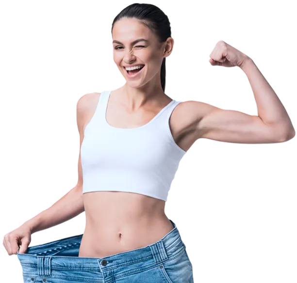 A fit woman in a white crop top confidently flexes her bicep while holding out the waistband of oversized jeans, suggesting significant weight loss or improved fitness.