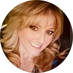 A close-up portrait of a smiling woman with long, wavy blonde hair, wearing makeup, including eyeliner and lipstick.