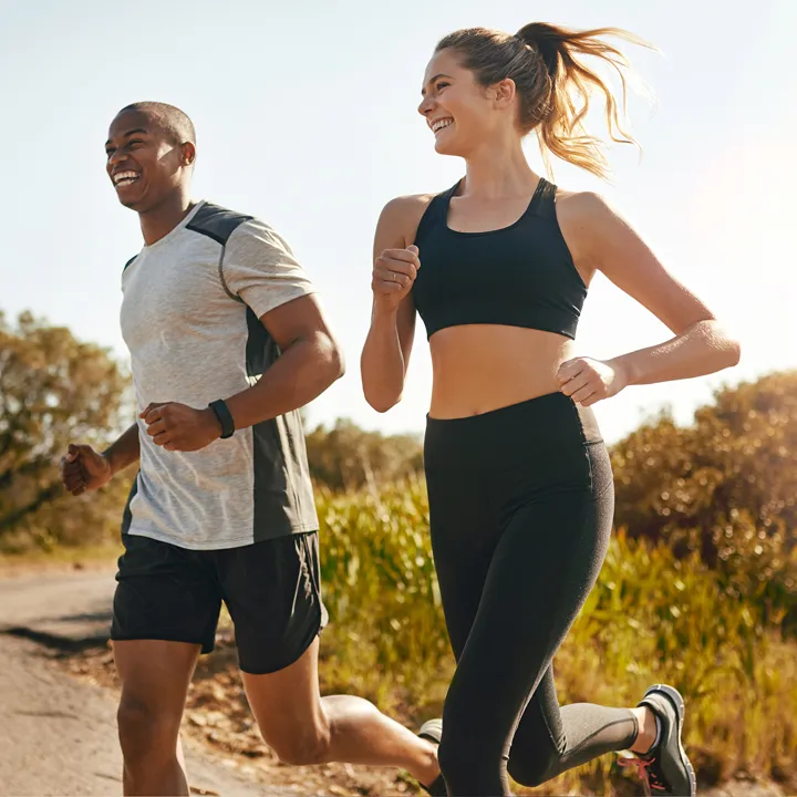 A man and a woman jogging outdoors on a sunny day, both wearing athletic attire and smiling.