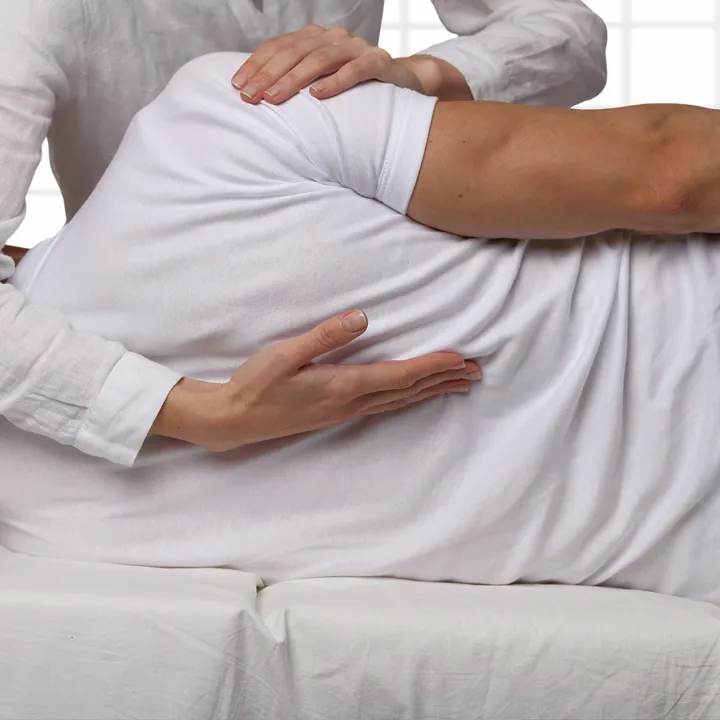 A physical therapist performs a spinal adjustment on a person lying on their side.